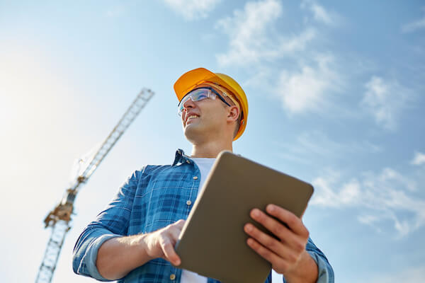 business, building, industry, technology and people concept - smiling builder in hardhat with tablet pc computer over group of builders at construction site
